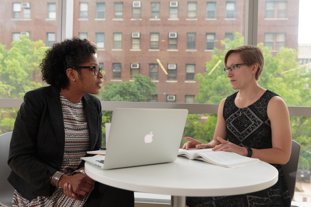 Two students sitting at a table talking to each other.
